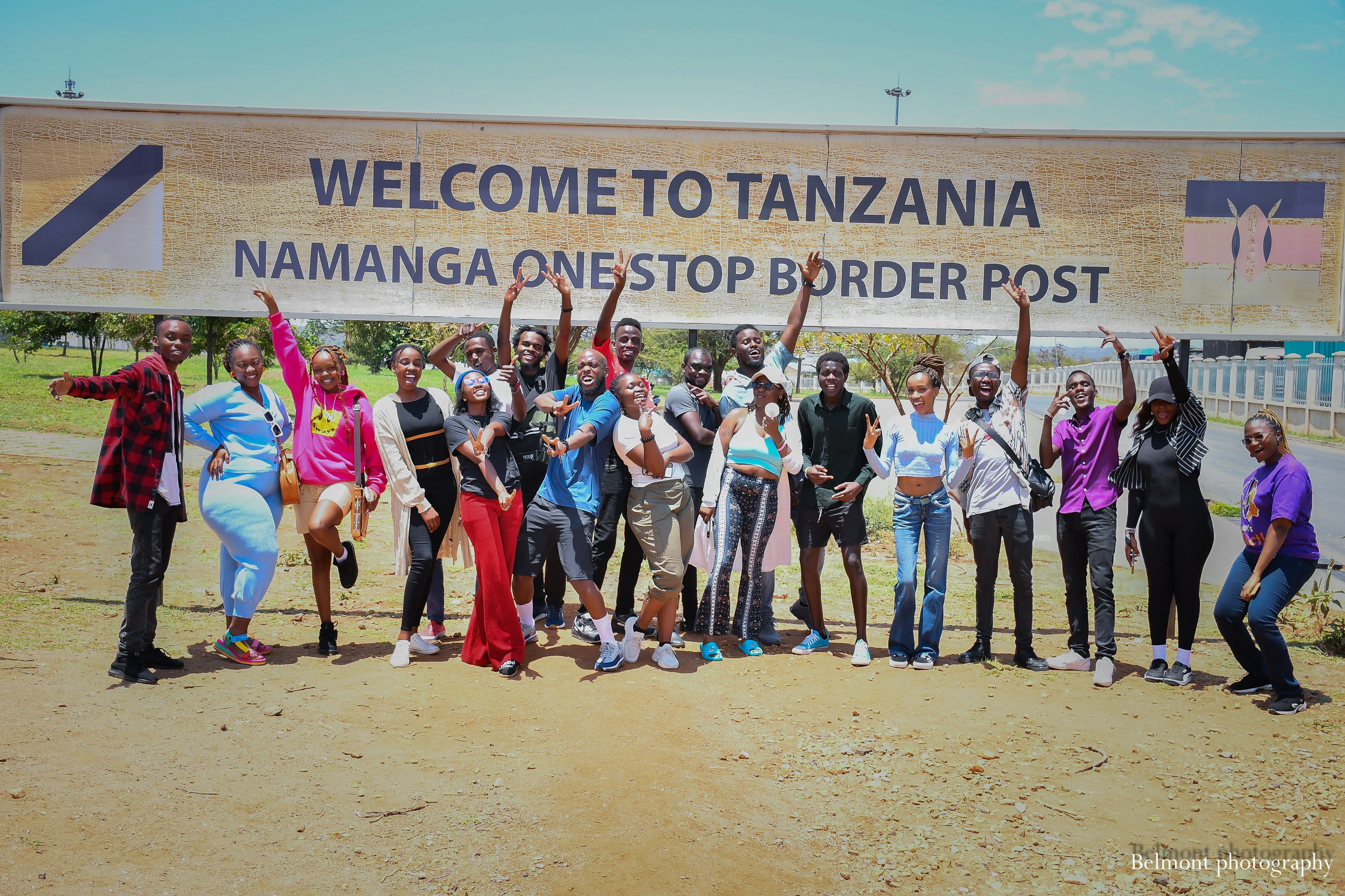 Young people laughing together beside a van on a scenic Kenyan highland road.